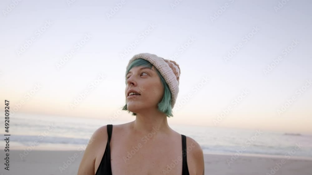 Mature woman standing on the beach looking around. Female in bikini and warm hat at the seashore during sunset. Mature woman standing on the beach looking around. Female in bikini and warm hat at the seashore during sunset.