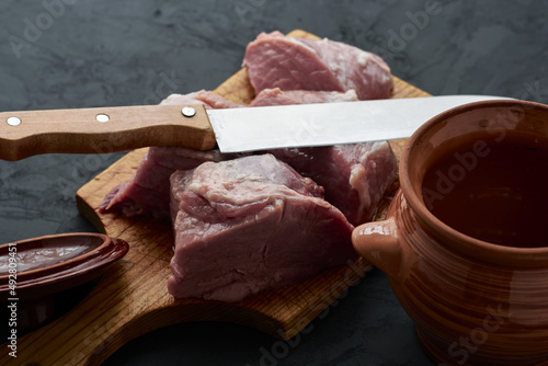 a piece of meat cut into pieces on a chopping board, a pot for chanakhi and a knife next to it photo