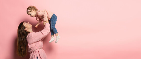 Play. Portrait of young woman and little girl, mother and daughter isolated on pink studio background. Mother's Day celebration. Concept of family, childhood, motherhood