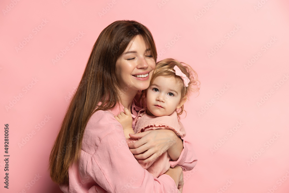 Huggins. Portrait of young woman and little girl, mother and daughter isolated on pink studio background. Mother's Day celebration. Concept of family, childhood, motherhood Huggins. Portrait of young woman and little girl, mother and daughter isolated on pink studio background. Mother's Day celebration. Concept of family, childhood, motherhood