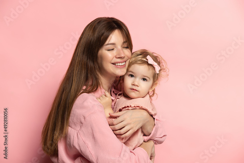 Huggins. Portrait of young woman and little girl, mother and daughter isolated on pink studio background. Mother's Day celebration. Concept of family, childhood, motherhood
