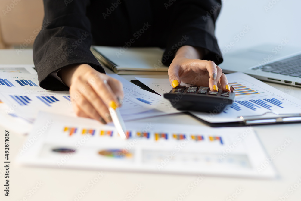 Businesswoman pointing at a business report chart and using a calculator for business analysis and auditing. Businesswoman pointing at a business report chart and using a calculator for business analysis and auditing.