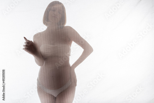 Pregnant woman in underwear touching fabric on grey background