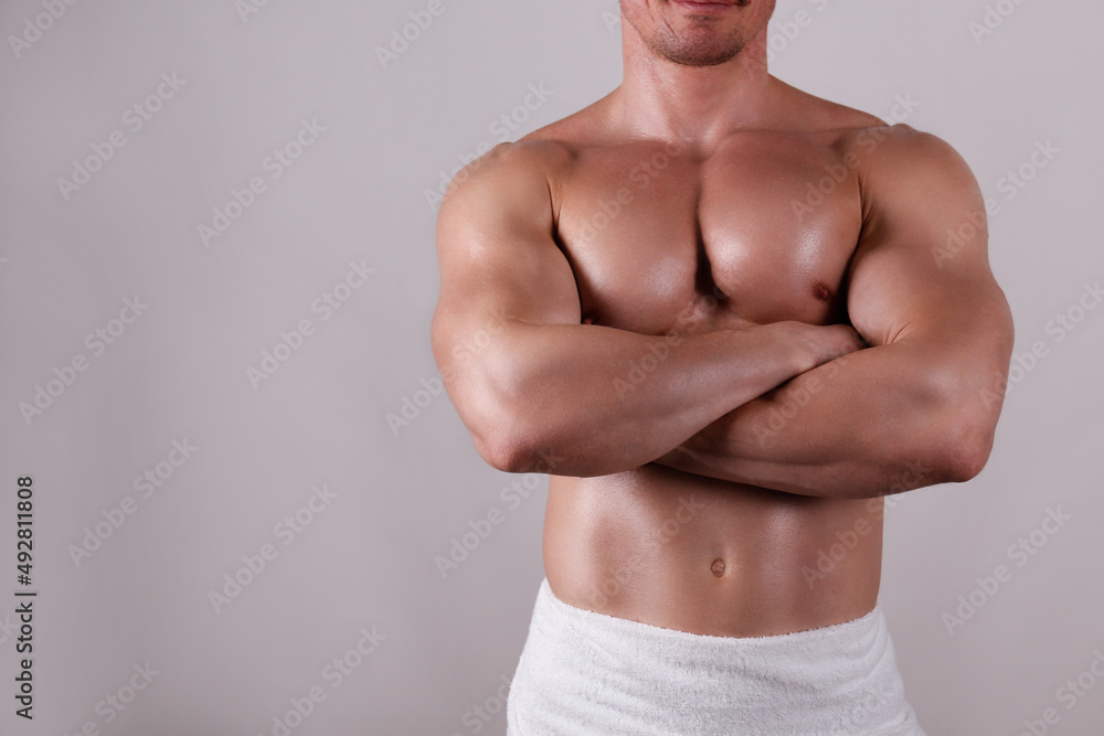 Professional bodybuilder wearing just a towel posing over isolated grey background. Studio shot of a shirtless fit guy flexing the muscles. Close up, copy space.