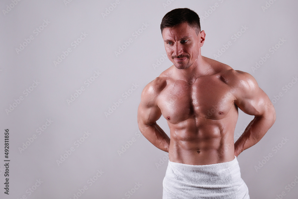 Professional bodybuilder wearing just a towel posing over isolated grey background. Studio shot of a shirtless fit guy flexing the muscles. Close up, copy space. Professional bodybuilder wearing just a towel posing over isolated grey background. Studio shot of a shirtless fit guy flexing the muscles. Close up, copy space.