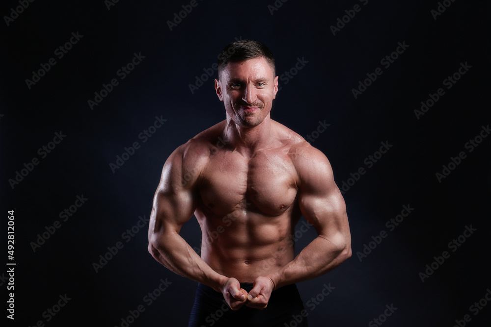 Professional bodybuilder posing over isolated black background. Studio shot of a fitness trainer flexing the muscles. Close up, copy space.