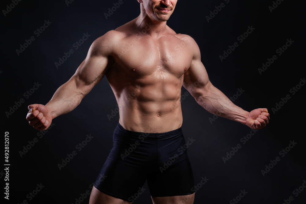 Professional bodybuilder posing over isolated black background. Studio shot of a fitness trainer flexing the muscles. Close up, copy space.