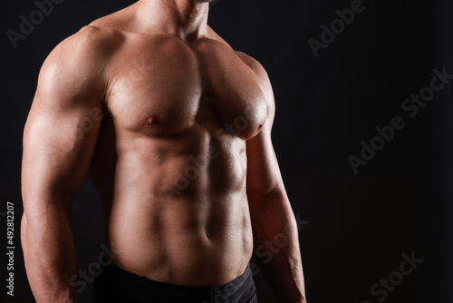 Professional bodybuilder posing over isolated black background. Studio shot of a fitness trainer flexing the muscles. Close up, copy space. © Evrymmnt