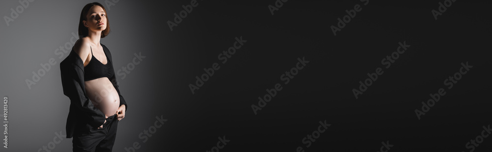 Pregnant woman in black top and blazer looking at camera on grey background, banner Pregnant woman in black top and blazer looking at camera on grey background, banner