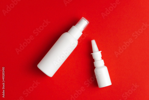Medicines for treatment of nose and throat. Nasal and throat spray bottles on red background. Mockup