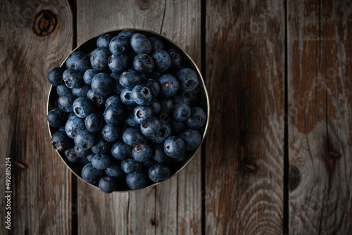 Bowl of fresh blueberries on rustic wooden table with copy space.