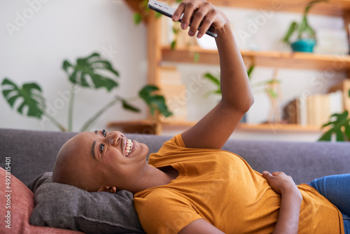 A young woman lies on the couch and looks up at her mobile phone