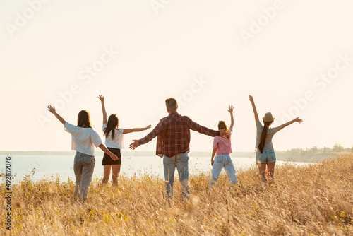 Group of happy friends stands with raised arms at sunset