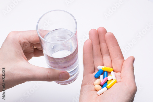 On a light background, male hands with pills and a glass of water. Medical concept
