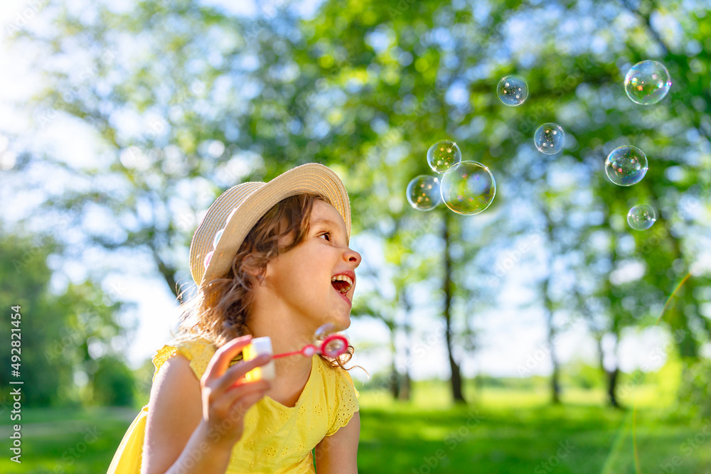 a carefree laughing girl blows soap bubbles on a bright sunny day.