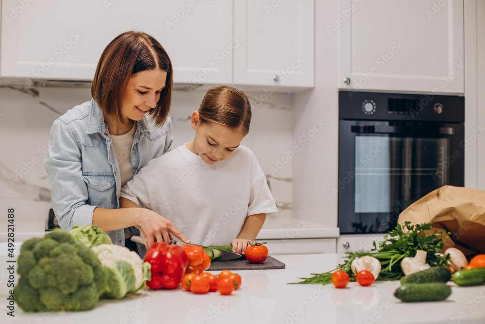 Mother with daughter preparing dinner from fresh vegetables at the kitchen Mother with daughter preparing dinner from fresh vegetables at the kitchen