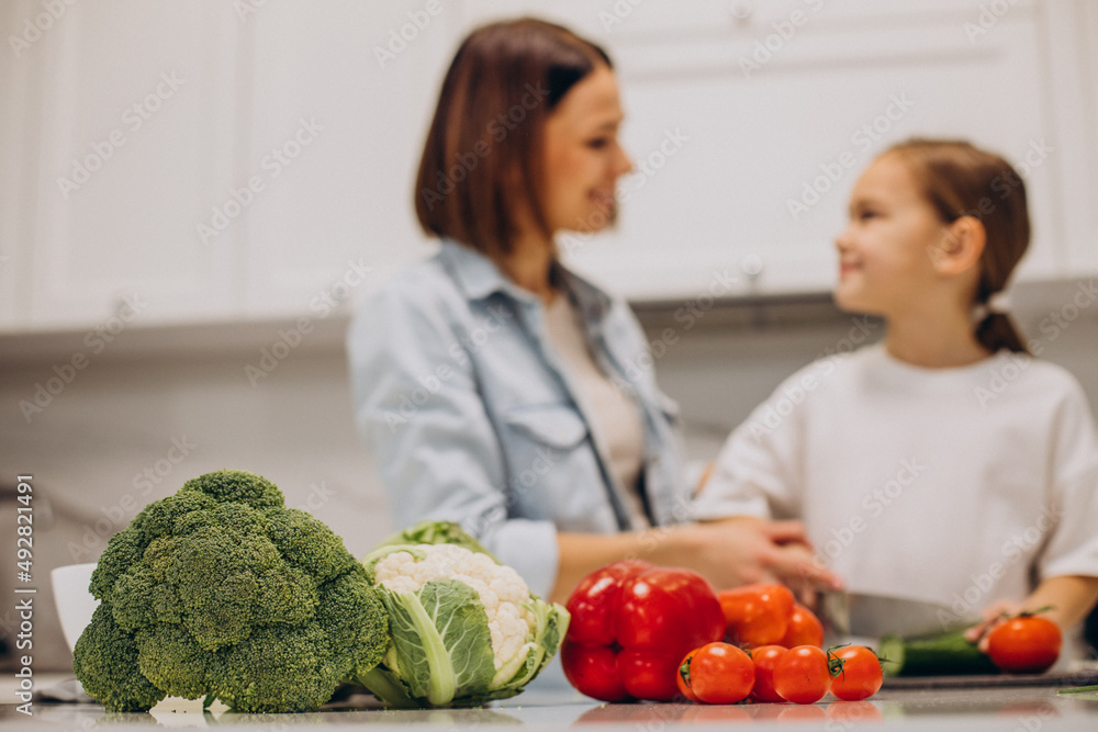 Mother with daughter preparing dinner from fresh vegetables at the kitchen Mother with daughter preparing dinner from fresh vegetables at the kitchen