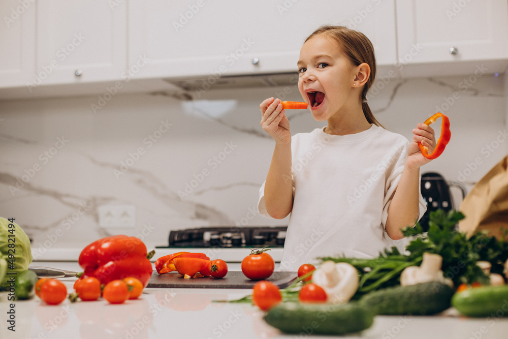 Little girl preparing salad at home at kitchen