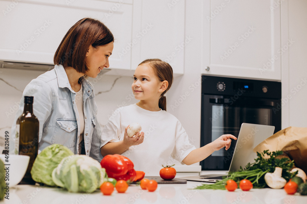 Mother with daughter preparing dinner from fresh vegetables at the kitchen