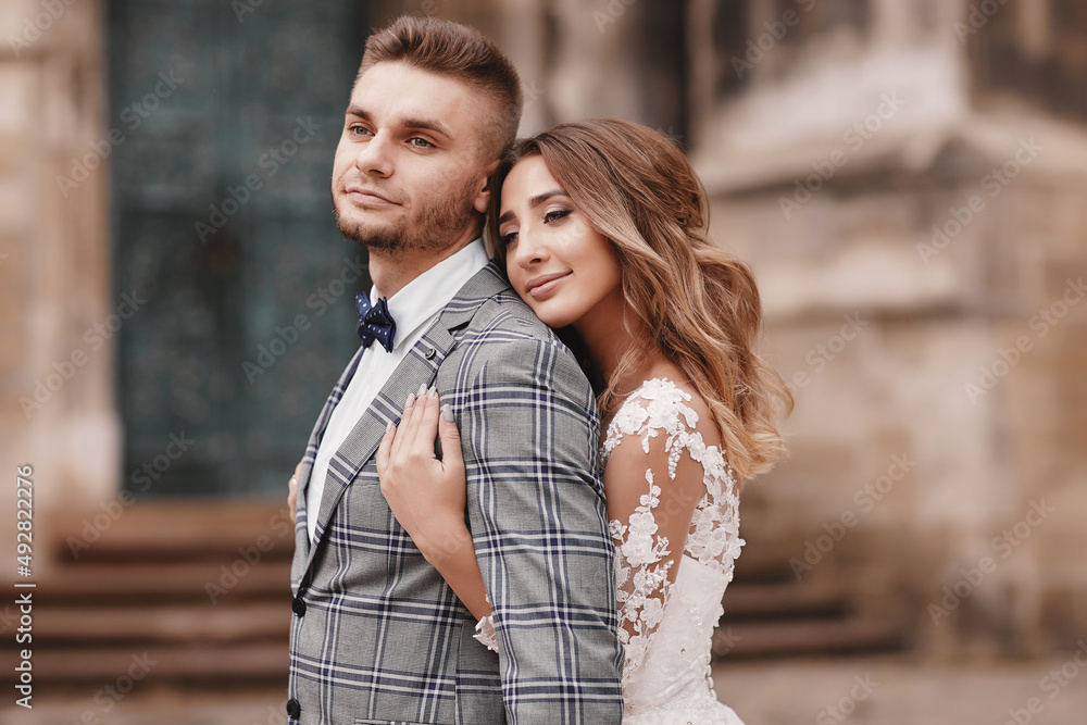 Stylish bride and groom gently hugging in european city street. Gorgeous wedding couple of newlyweds embracing near ancient building. Romantic moment. wedding day