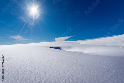 Beautiful winter landscape with powder snow against a clear blue sky with clouds and sun rays. Lessinia Plateau Regional Natural Park (Altopiano della Lessinia) Verona Province, Veneto, Italy, Europe.
