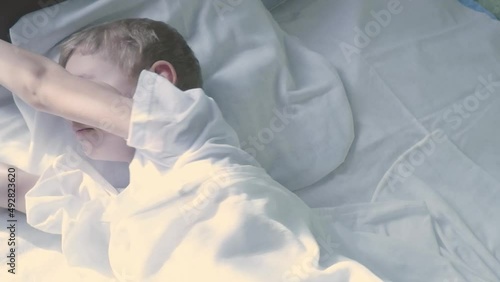 A small seven year old Caucasian boy wakes up, stretches and smiles in a white bed. photo