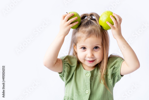 a cute little baby girl is holding a big green apple in her hands. White isolated background. Healthy foods for children or a healthy snack. Space for text. High-quality photography