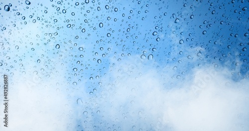 Rain drops on blue glass window with fog background.