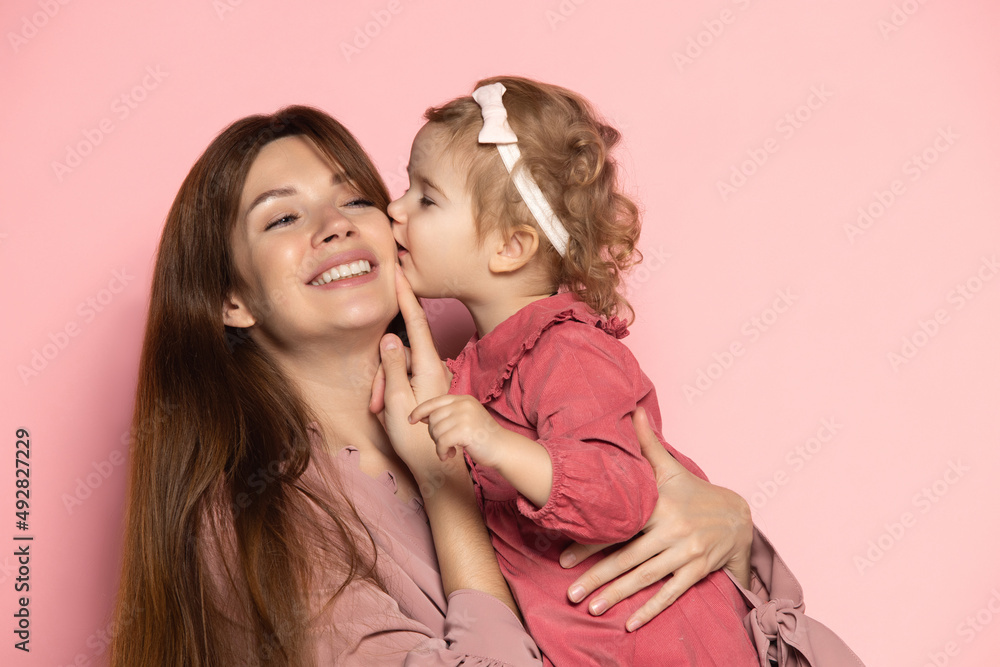 Delighted young woman and toddler, caring mother and daughter isolated on pink studio background. Mother's Day celebration. Concept of family, childhood, motherhood Delighted young woman and toddler, caring mother and daughter isolated on pink studio background. Mother's Day celebration. Concept of family, childhood, motherhood