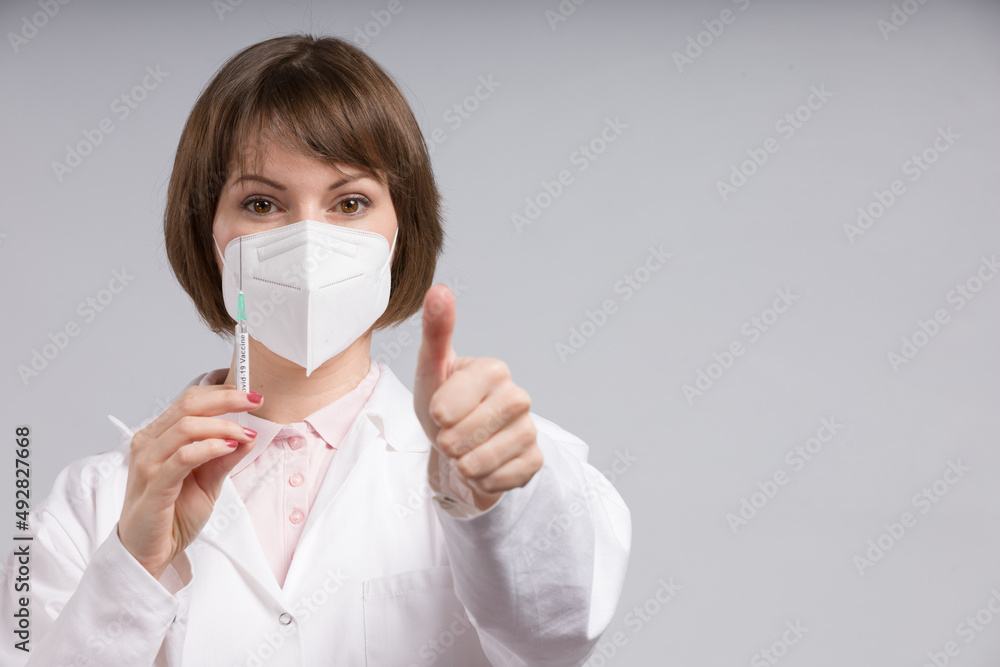 female doctor or nurse with syringe pulled up with a vaccination serum shows thumbs up female doctor or nurse with syringe pulled up with a vaccination serum shows thumbs up