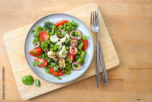 Vegetable meal from green beans, peas, and spinach with braised onions, feta cheese and tomatoes for a vegetarian low carb diet on a wooden table, copy space, top view from above