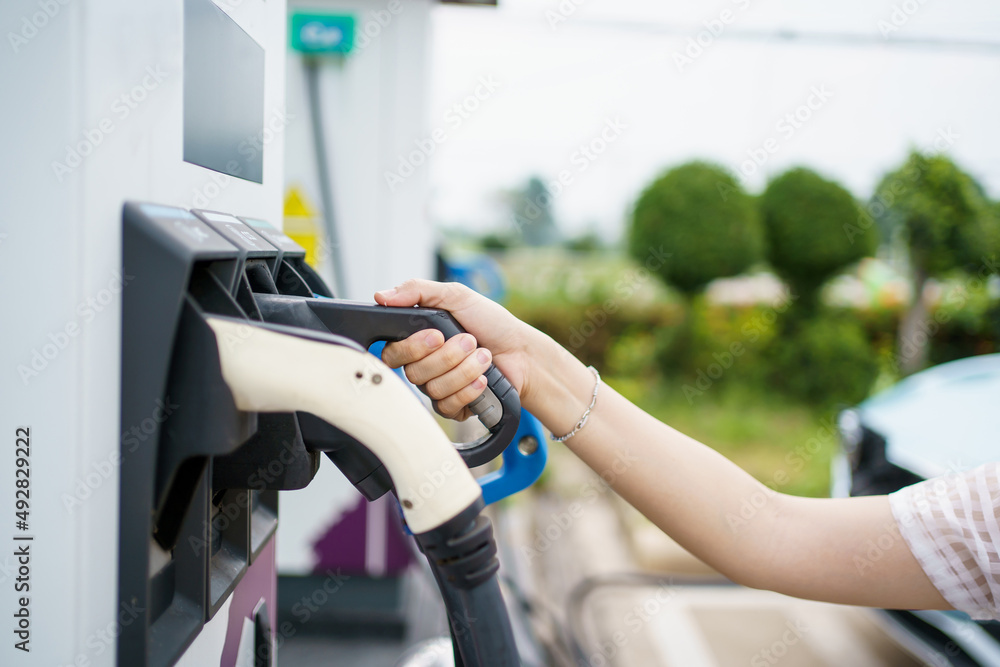 Happy Asian woman holding a DC - CCS type 2 EV charging connector at EV ...