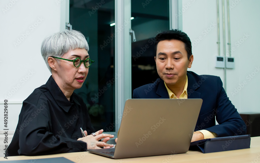 Fototapeta premium Senior aging businesswoman and young adult handsome smart businessman working overtime together at night, using laptop for creative project marketing plan, smiling with confidence and happiness.
