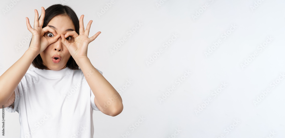 Funny young asian woman, korean girl making eyes glasses gesture, looking  happy at camera, standing over white background Stock Photo | Adobe Stock