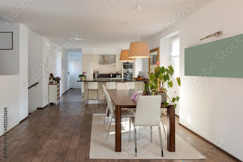 Open space with leather table and chairs and a modern kitchen with island and stools in the background