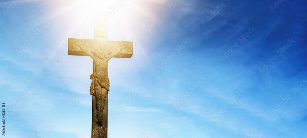 Easter religious background greeting card - Crucifixion and resurrection of Jesus Christ at Golgota (Golgotha), crucifix with jesus christ, blue cloudy sky and bright shining sunshine over cross