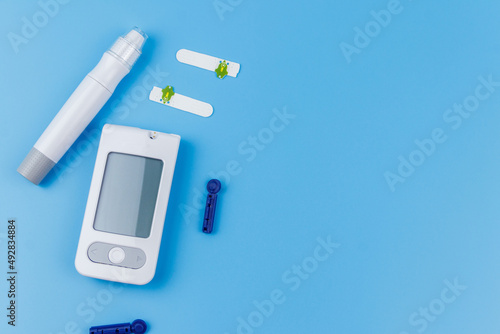 Digital glucometer, lancet pen, disposable needles and test strips on pastel blue background. Top view, copy space. Diabetes concept