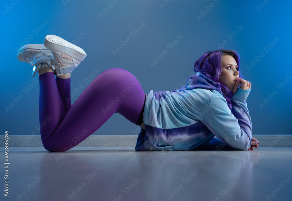 a girl in stylish purple sportswear and with purple hair is sexy lying on the floor - obrazy, fototapety, plakaty 