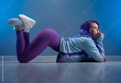a girl in stylish purple sportswear and with purple hair is sexy lying on the floor photo