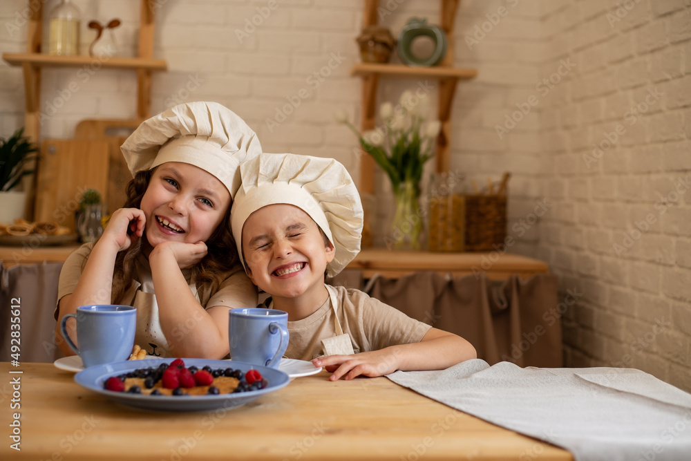cute little children are sitting at a wooden table, leaning on their elbows and laughing merrily cute little children are sitting at a wooden table, leaning on their elbows and laughing merrily