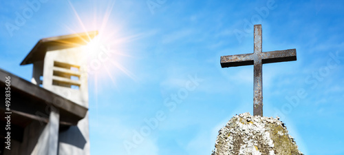 Religious Background - Blue sky with old weathered cross on rock on cemetery or church, illuminated by the sun photo