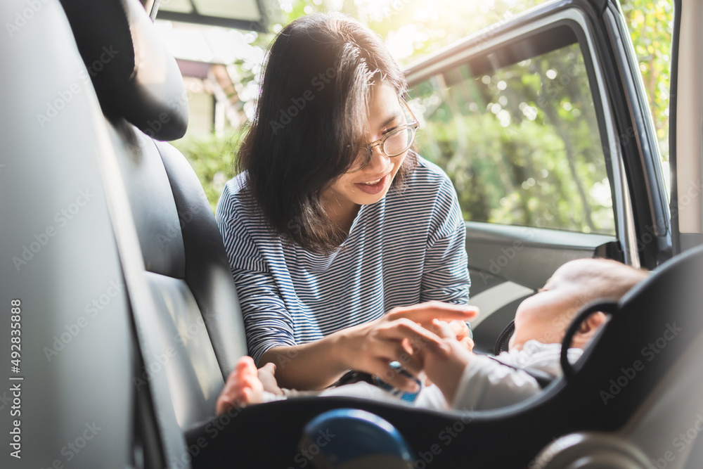 Asian Young Mother putting her baby boy on safety child car seat Asian Young Mother putting her baby boy on safety child car seat