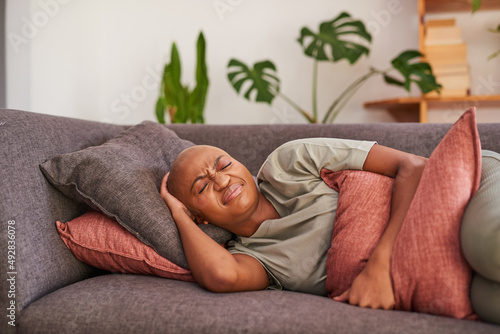 A young woman clutches her stomach in pain while she rests on the sofa at home photo