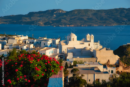 View of Plaka village on Milos island over red geranium flowers on sunset. Plaka town  Milos island  Greece. Focus on flowers