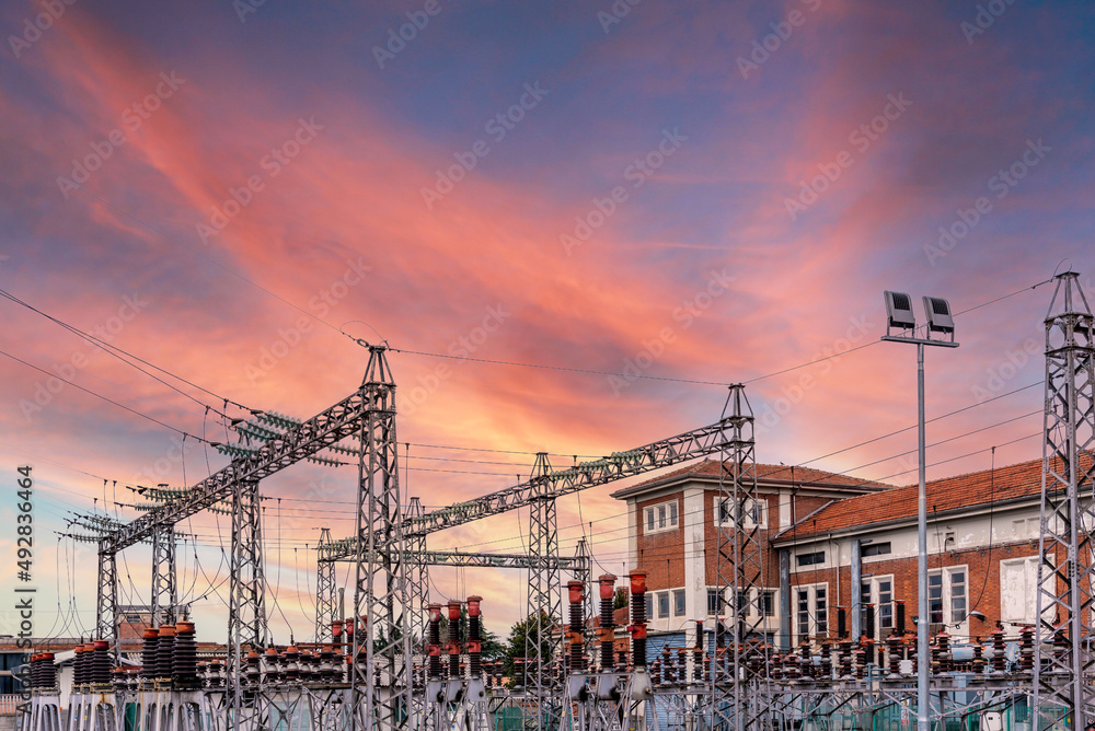 Electric transformer station with pylons with high voltage cables, colorful sunset sky, expensive energy cost concept