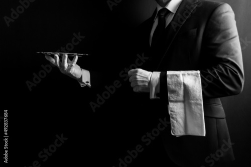 Portrait of Butler or Waiter in Dark Formal Suit and White Gloves with Napkin Over Arm Holding Silver Serving Tray.