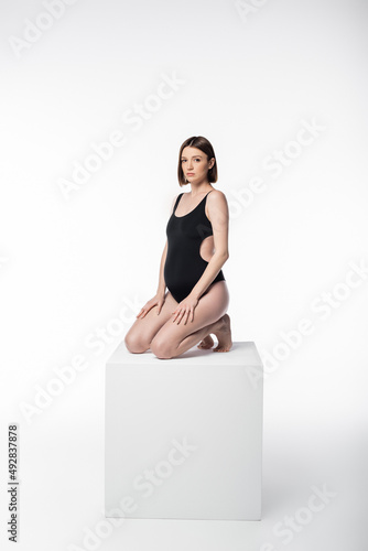 Pregnant woman in swimsuit posing on cube on white background