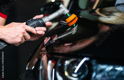 Close up of car detailist hands, cleaning or pilishing the car by poliermaschine, car detailing concept, orbital polisher in repair shop polishing car