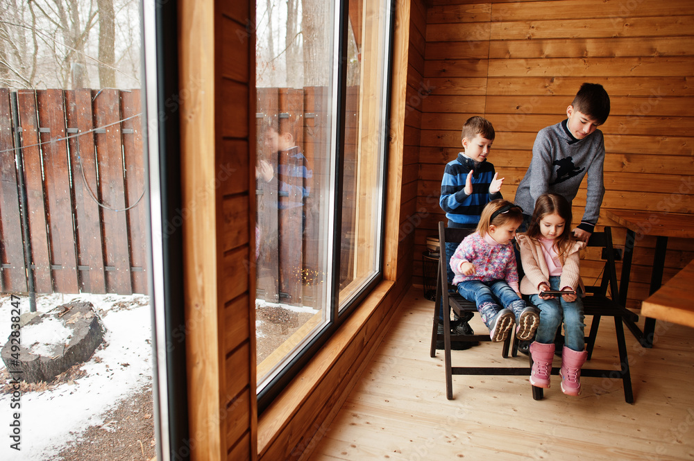 Four kids in modern wooden house watching video in mobile phone.