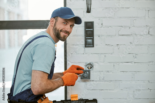 Cheerful young man fixing electrical wall socket photo